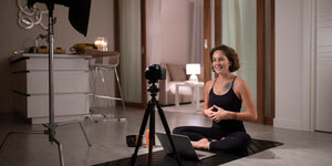 Eine Yogalehrerin spricht in ihr Heimstudio-Setting mit Yogamatte, Kamera, Licht und Laptop