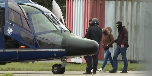 Eine Frau in einer Kapuzenjacke mit Fellrand wird zu einem Hubschrauber geführt
