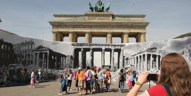 Touristen und Touristinnen am Brandenburger Tor vor einer Panorama-Fotografie aus der Zeit des 2. WEltkriegs