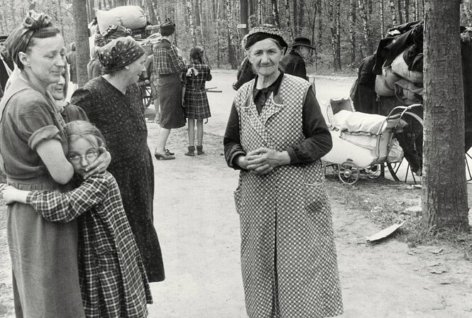 Frauen in Kittelschürzen stehen in einem Park, ein Mädchen schmiegt sich an eine ältere Frau