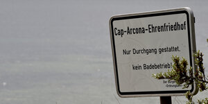 Ein Schild steht an einem Strand. Auf dem Schild steht: Cap-Arcona-Ehrenfriedhof