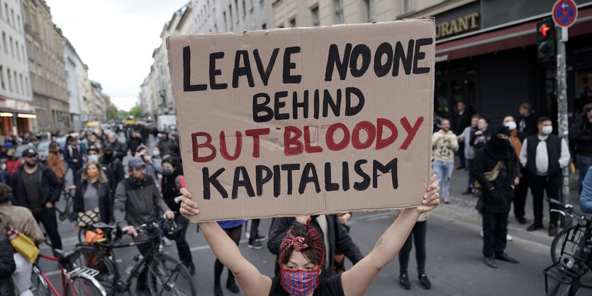 Frau mit Pappschild "Leave no one behind but bloody kapitalism"