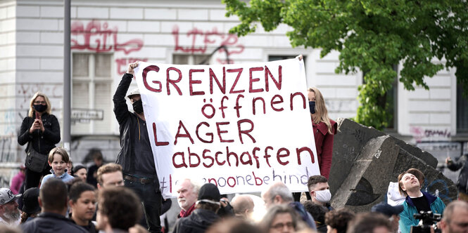 Auf einem transparent in einer Menschenmenge steht: Grenzen öffnen.Lager abschaffen