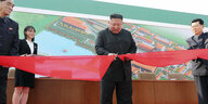 Kim Jong Un zerschneidet ein recht breites rotes Band, an der Seite stehen Menschen, dahinter ein großes Wandgemälde der Düngemittelfabrik