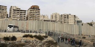 Häuser hinter einer Mauer, im Vordergrund Menschen