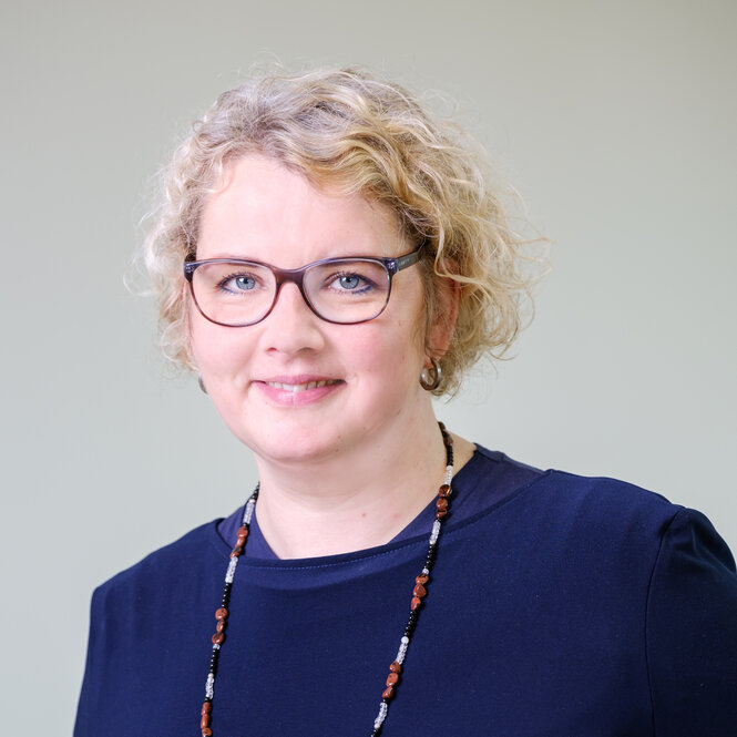 Ein Portraitfoto von Maike Finnern. Sie hat blonde Locken und trägt eine Brille