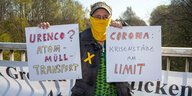 eine Frau mit einem Tuch vor dem Mund hält zwei Schilder gegen Atommüllexporte hoch