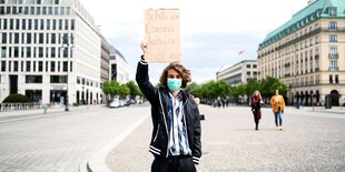 Ein Mann mit einem Schild auf dem "Schutz vor Corona, auch für Flüchtlinge" steht.