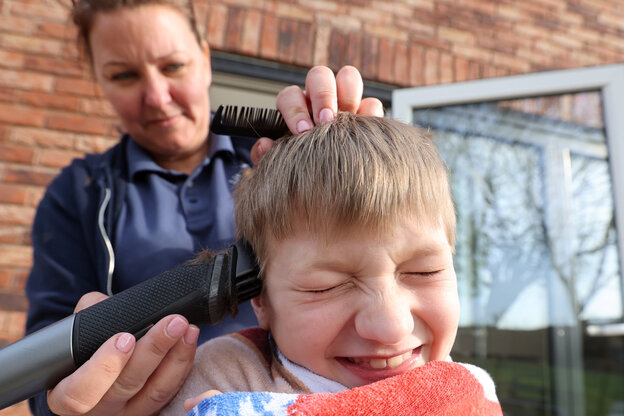 Frau schneidet einem Kind Zuhause mti einem Haarschneider die Haare