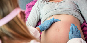 eine Hebamme mit blauen Schutzhandschuhe untersucht den Bauch einer Schwangeren