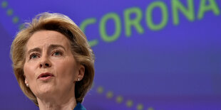 Von der Leyen vor einer blauen Wand, auf der in in grünen Buchstaben "Corona" steht