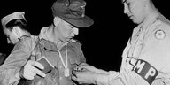 Ein amerikanischer Soldat nimmt einem deutschen Soldaten einen Orden ab.