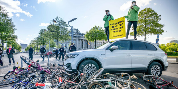 tivisten von Greenpeace demonstrieren vor dem Reichstag mit einer Aktion, bei der ein Auto über Fahrräder fährt.
