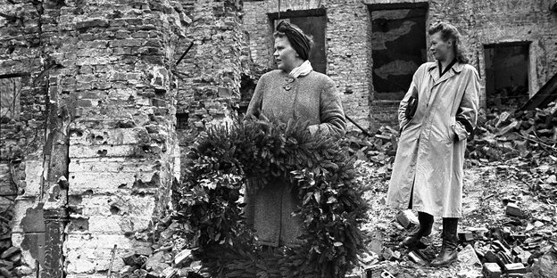 Zwei Frauen stehen mit einem Kranz in den Trümmern von Warschau im 2. Weltkrieg