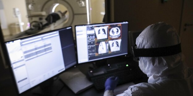 Ein Arzt sitzt vor zwei Compumterbildschirmen und werte eine Tomographie aus