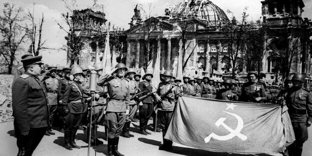 Sovietische Soldaten mit Flagge vor dem zerschossenen Reichstag.