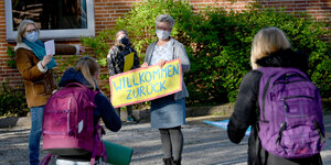 Lehrerin begrüßt Schüler mit Schild