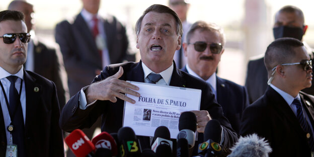 Brasiliens Präsident Bolsonaro mit einer Zeitung in der Hand vor einer Versammlung."Hal