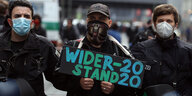 Ein Demonstrant wird am Rande einer Demonstration von Polizisten mit Mundschutz abgeführt, während er ein Schild hält mit der Aufschrift "Widerstand – 2020".