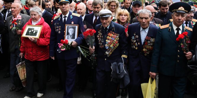 Menschen, teilweise in Uniform, halten zum Gedenken alte Portraitfotos in ihren Händen.