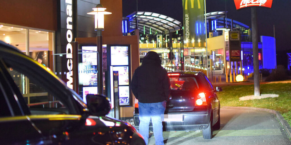 Eine Person steht zwischen Autos an einem McDrive-Schalter.