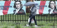 Eine Frau mit Regenschirm läuft an Wahlplakaten vorbei.