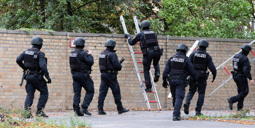 Spezialkräfte der Polizei steigen über eine Mauer.