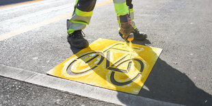 Ein Bauarbeiter sprüht ein Fahrradsymbol auf die Straße.