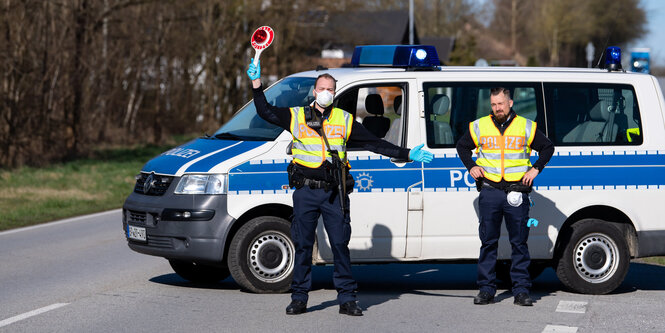 Zwei Polizisten stehen auf einer Straße und stoppen den Verkehr.