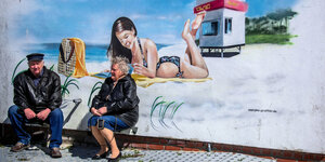 Ein Rentnerpaar sitzt vor einem Graffiti mit einer Strandszene