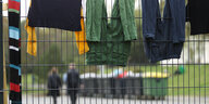 Sicherheitskräfte laufen auf dem Gelände des Flüchtlingsheim während Wäsche zum Trocknen über einem Zaun hängt – ein Symbolbild
