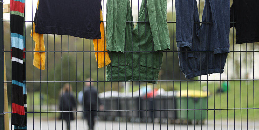 Sicherheitskräfte laufen auf dem Gelände des Flüchtlingsheim während Wäsche zum Trocknen über einem Zaun hängt – ein Symbolbild