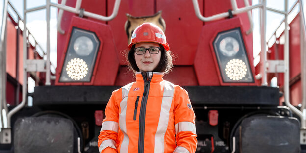Eine Lokführerin mit Helm steht vor einer Lokomotive.