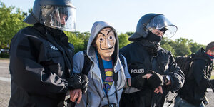 Ein Demonstrant mit Maske wird von zwei Polizisten abgeführt.