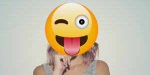 Eine Frau hält sich einen Emoji vors Gesicht.