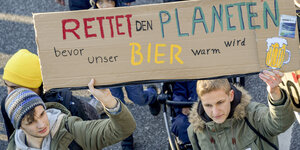 Jugendliche halten ein Schild hoch, darauf steht "Rettet den Planeten, bevor unser BIer warm wird"
