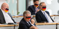 Vier Landtagsabgeordnete der sächsischen AfD-Fraktion sitzen mit Schwarz-rot-goldenen Schutzmasken im Plenarsaal