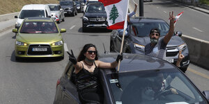 Ein Autokorso. Beim vordersten Auto ragen im Fahren eine Frau und ein Mann aus dem Fenster. Sie schwenkt die libanesische Fahne