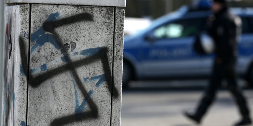 Auf Verteilerkasten gesprühtes Hakenkreuz, im Hintergrund geht ein Mann