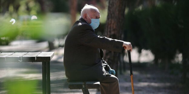 Ein älterer spanischer Mann sitzt mit Mundschutz auf einer Parkbank in Madrid