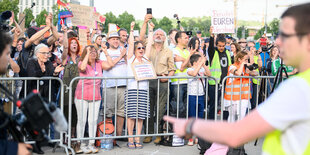 Dicht gedrängt hinter einem Absperrgitter stehende Menschne. Einer hält ein Schild hoch, auf dem steht: benutzt euren Verstand.