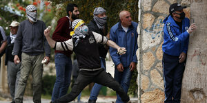 Ein vermummter Demonstrant wirft einen Stein