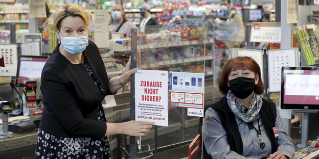 eine Frau, die Ministerin, steht neben einer Supermarktkassierin