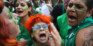 Mehrere Frauen, zum Teil mit bemalten Gesichtern, rufen erregt Slogans.