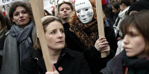 Frauen marschieren mit Masken und Schildern gegen häusliche Gewalt