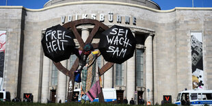 Vor der Volksbühne lehnt eine Frau am Räuberrad mit zwei Schirmen in der Hand