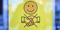 Ein Schild zeigt ein freundlich lächelndes Gesicht und zwei durchgestrichen Hände, die zum Gruß gereicht werden