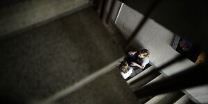 Ein dunkles Treppenhaus - in einem Sonnenlichtstrahl sitzen zwei Jugendliche im Gespräch vertieft - eine Einrichtung der Jugendhilfe in Berlin