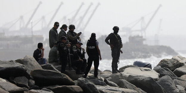Soldaten stehen auf Felsen am Meer. Im Hintergrund ein Hafen.