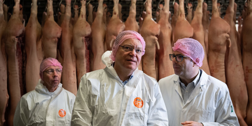 Drei Männer in Schutzanzügen vor Schweinhälften